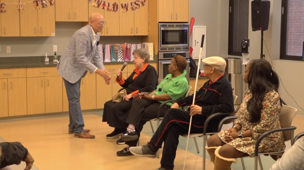 Todd giving the microphone to Gail Synder, the narrator for Do the proper thing, please ask, do not assume.